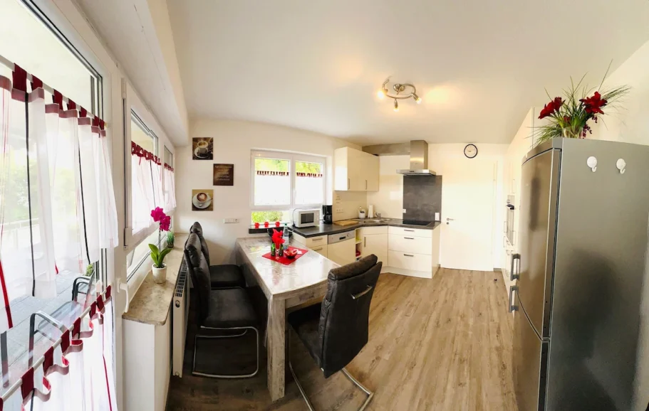 Moderne Küche mit Tisch, Stühlen, Kühlschrank und hellen Wänden. Blumen dekorieren den Raum.